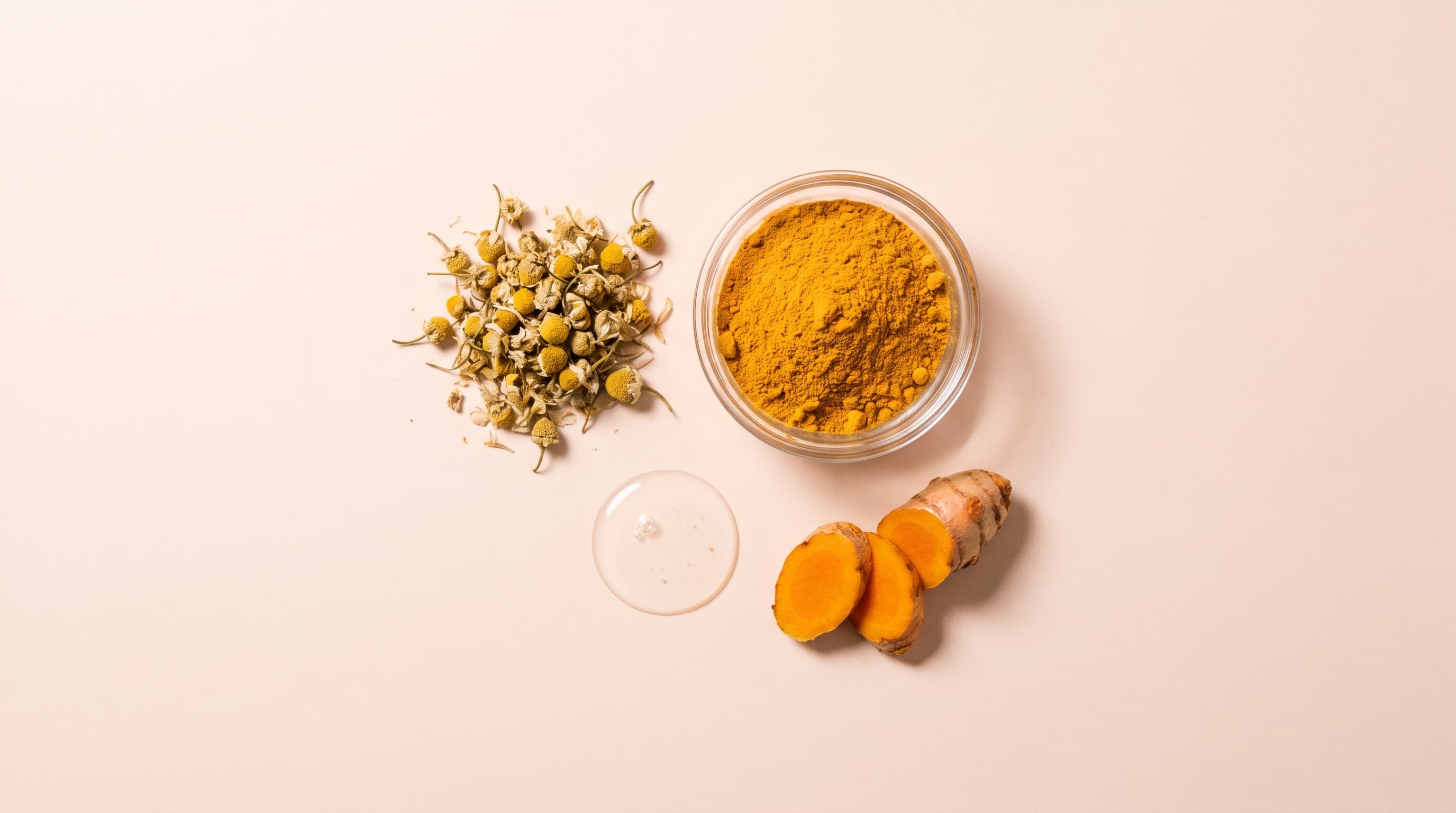 Fresh turmeric, chamomile flowers and a serum dropper laid out together