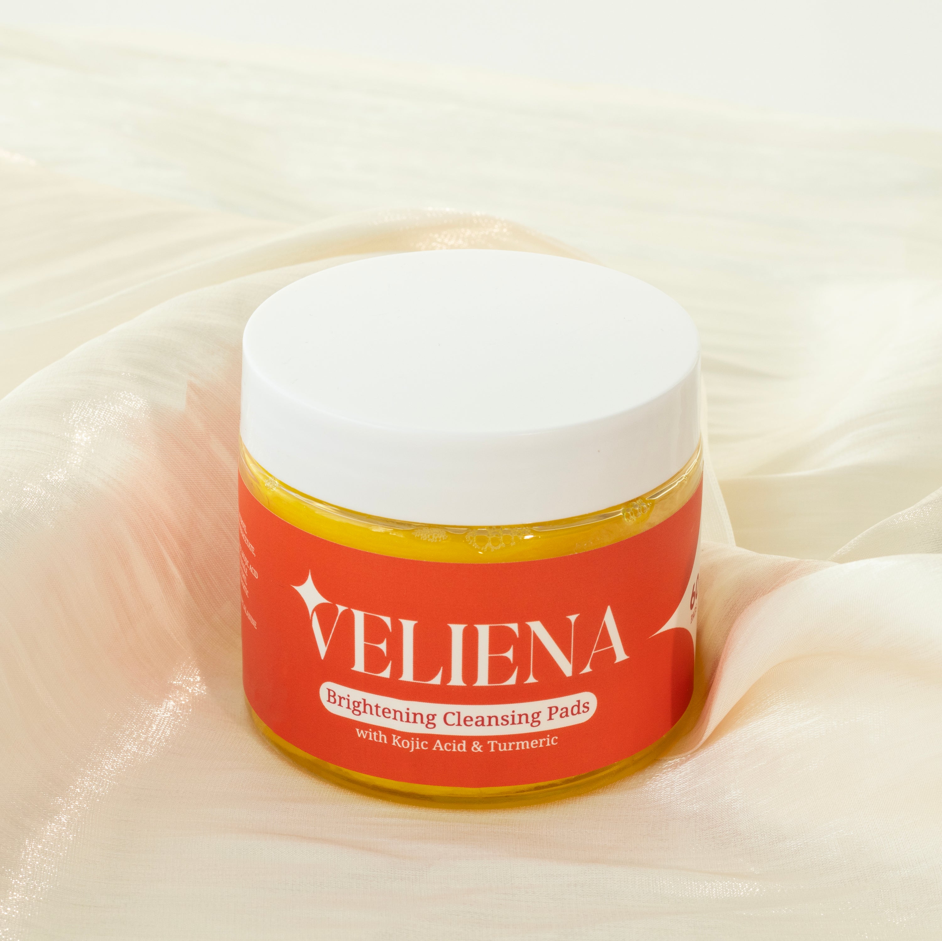 Jar of Veliena Brightening Cleansing Pads on a beige fabric background
