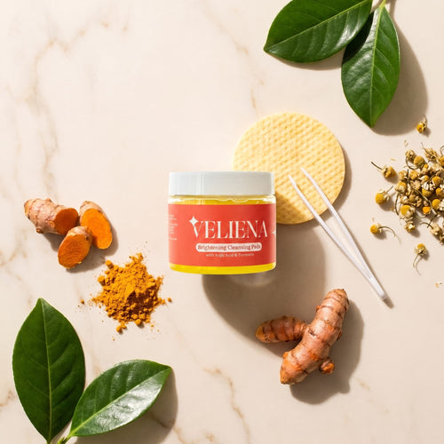 Veliena Brightening Cleansing Pads jar with its hygienic tweezers, fresh turmeric root and chamomile flowers on marble